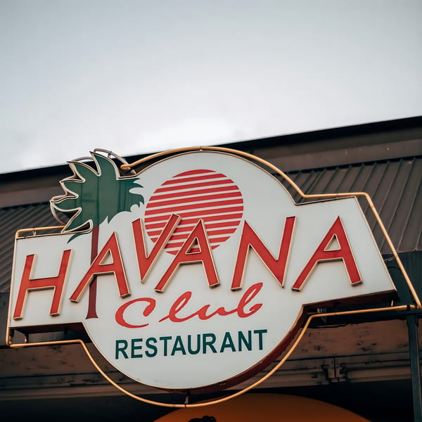 Havana Club Restaurant & Bar sign with a palm tree and sun logo against a cloudy sky.
