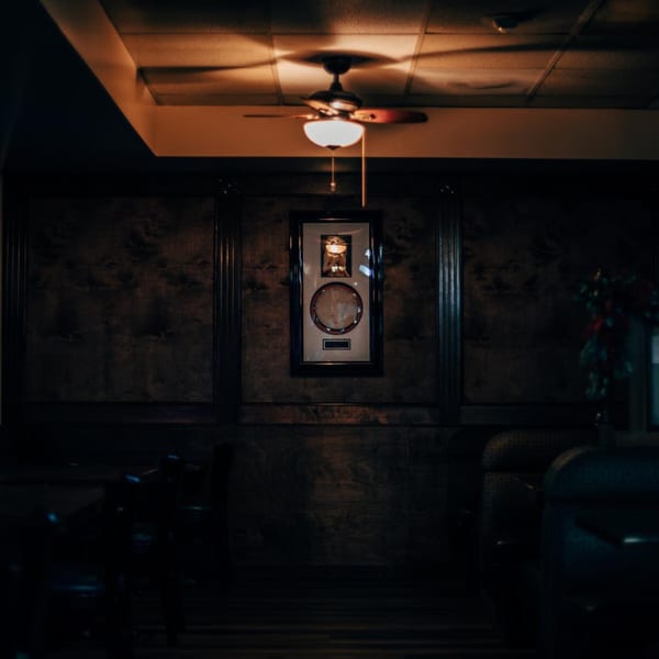 Dark, moody interior of Havana Club with a lit ceiling fan and framed artwork on a wood-paneled wall.