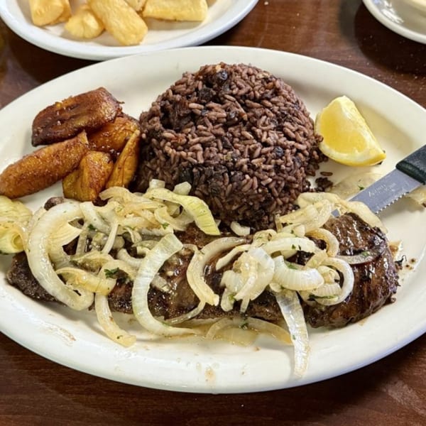 Cuban steak with sautéed onions, rice and beans, fried plantains, and a lemon wedge.