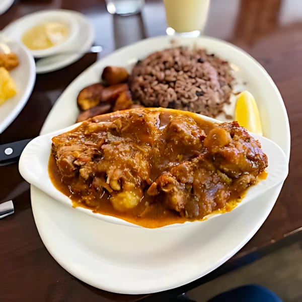 Cuban-style stewed meat with rice, plantains, and a lemon wedge on a white plate.