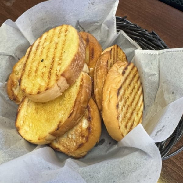 A basket of toasted Cuban bread slices with grill marks, lined with white parchment paper.