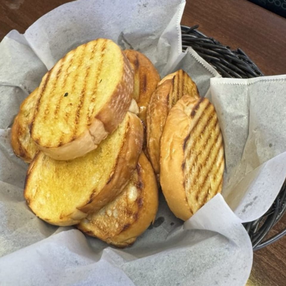 A basket of toasted Cuban bread slices with grill marks, lined with white parchment paper.