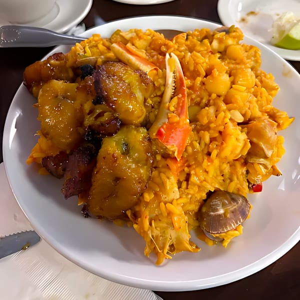 A vibrant Cuban seafood paella with rice, crab claws, plantains, and clams on a white plate.
