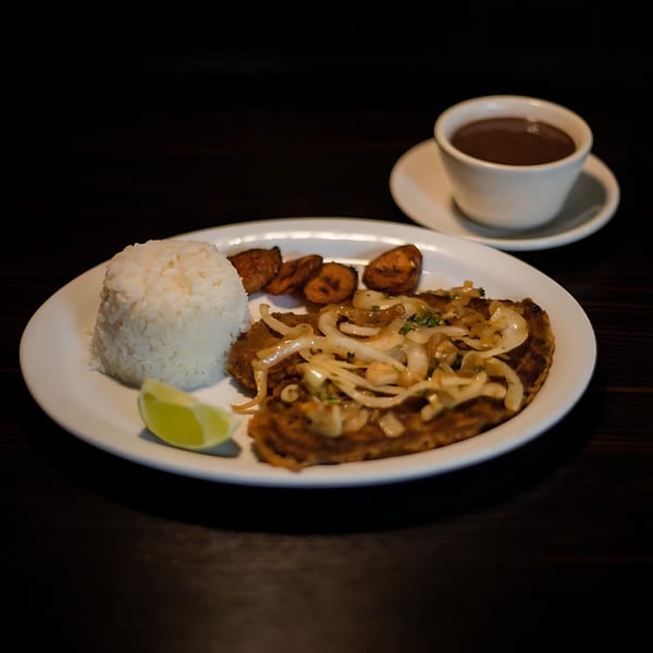 Cuban steak with onions, white rice, fried plantains, lime, and a cup of coffee.