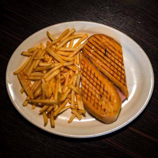 A Cuban sandwich with grill marks and a side of golden french fries on a white oval plate.