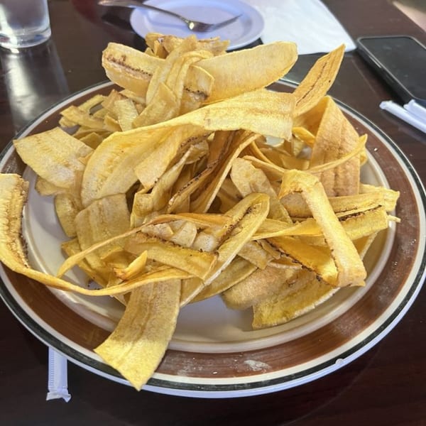 A large plate of golden-brown, thinly sliced plantain chips, a Cuban specialty, on a dark table.