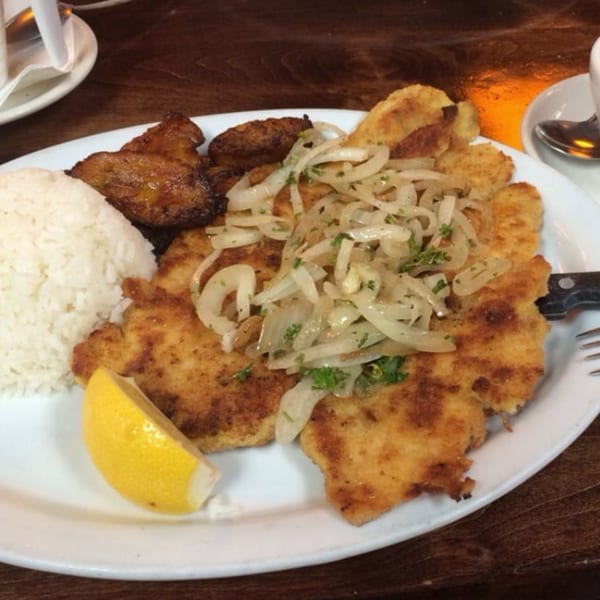 Cuban breaded steak topped with onions, served with white rice, fried plantains, and a lemon wedge.