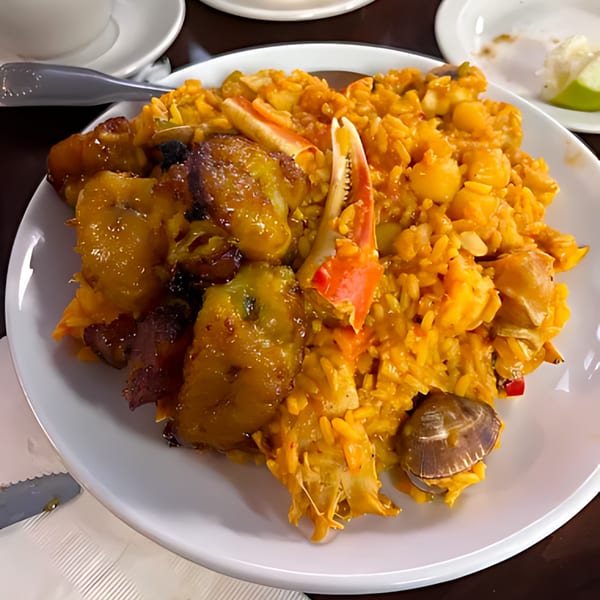 Cuban seafood paella with rice, crab claws, plantains, and clams on a white plate.