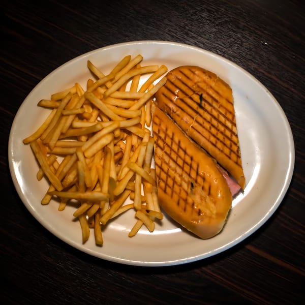 A Cuban sandwich with grill marks and a side of golden french fries on a white oval plate.