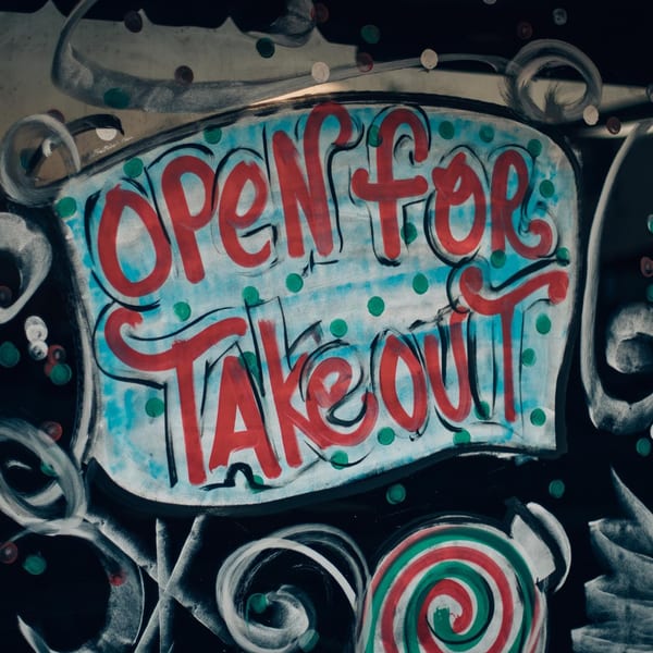 A hand-painted sign on a window reads "Open for Takeout" in red letters on a blue background.
