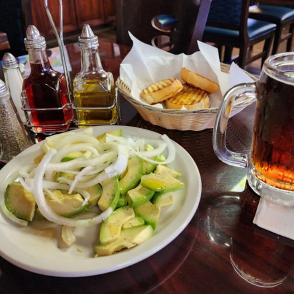Cuban avocado and onion salad, grilled bread, and a beer on a dark wooden table.