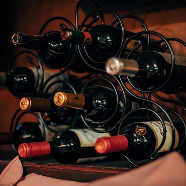 Wine bottles with red and gold foil tops stored in a black metal wine rack.